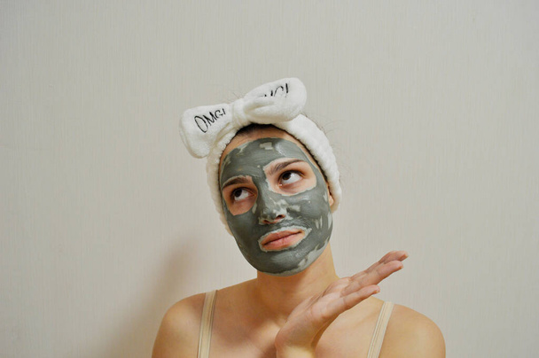 Девушка с повязкой на голове и глиняной маской на лице на белом фоне - Фото, изображение