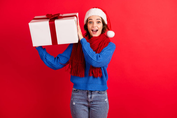 Photo of astonished girl in santa claus headwear get christmas jolly advent gift box impressed shake wear blue knitted pullover denim jeans isolated over bright shine color background - Fotoğraf, Görsel