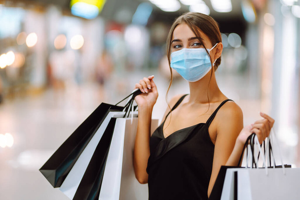 Fashionable woman in protective  medical mask with shopping bags walking in the mall. Shopping during the coronavirus Covid-19 pandemic. Purchases, black friday, discounts, sale concept.  - Фото, зображення