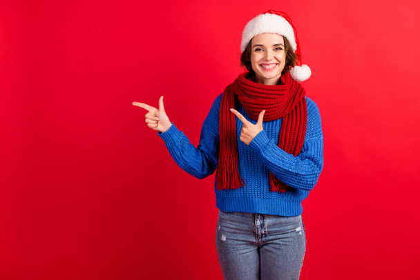 Photo of positive girl in santa claus cap point index finger demonstrate christmas tradition magic discount wear blue knitted pullover jeans isolated over bright shine color background - Foto, afbeelding