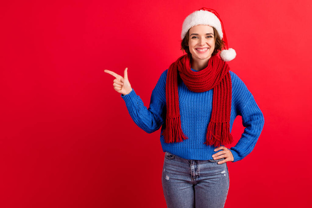 Photo positive girl in santa claus cap point index finger copyspace demonstrate christmas tradition discount promotion ads wear blue sweater jeans isolated bright shine color background - Fotografie, Obrázek