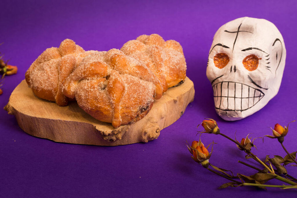 Day of the dead, mexican tradition concept with dead bread, sugar skull and dry flowers on violet background - Photo, Image