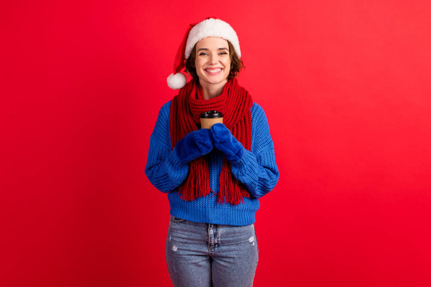 Positive girl in santa claus cap hold hot coffee beverage takeout mug enjoy christmas x-mas noel weekend holiday wear denim mittens knitted pullover isolated bright shine color background - Foto, afbeelding