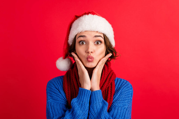 Portrait amazed funny cute girl in santa claus headwear impressed christmas magic discounts touch hands face cheeks cheekbones wear blue sweater isolated red bright color background - Foto, imagen