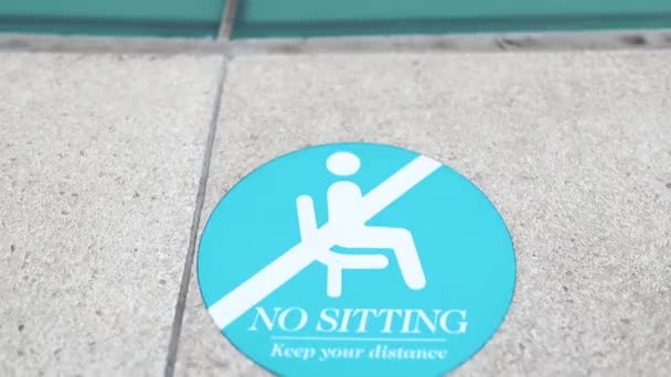 Un letrero redondo de "No sentarse" debido a Covid 19 en la acera - Imágenes, Vídeo