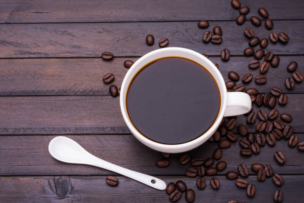 Sötét kávé fehér kávéscsészében és pörkölt kávébab elhelyezve egy fekete fa asztalon, és van hely a szöveges tervezés. - Fotó, kép