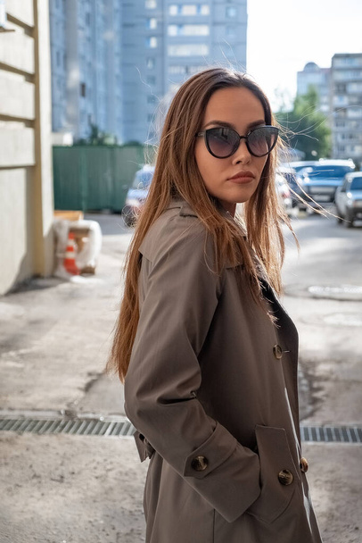 atraktivní mladý asijský model v šedém trench kabát stojící v blízkosti zdi venku - Fotografie, Obrázek
