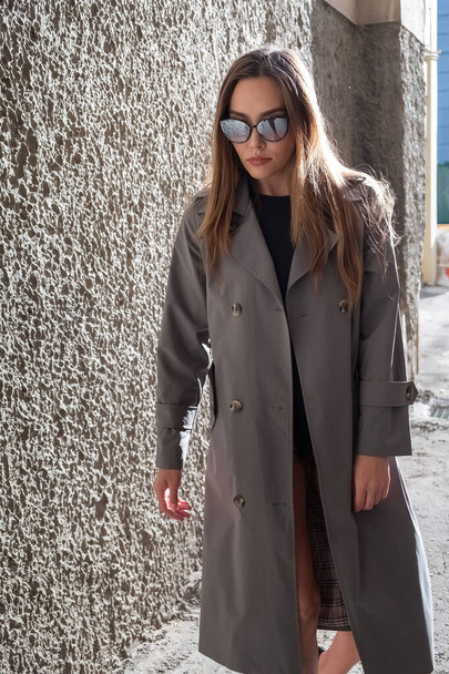 attractive young asian model in gray trench coat standing near wall outdoors - Photo, Image