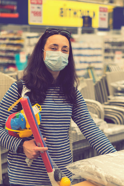 La mujer con la máscara protectora en el supermercado escoge los juguetes infantiles. tonificado. foto vertical. tonificado. - Foto, imagen