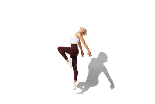 Beautiful young female athlete practicing on white studio background with shadow - Foto, imagen