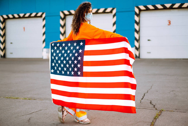 Portrait of a young  woman wearing a protective mask and holding a USA flag in the street city. Freedom and memorial concept. Covid-2019. - Fotoğraf, Görsel