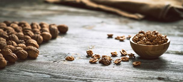 Fresh walnut kernels and whole walnuts in a bowl on rustic old wooden table. Healthy organic food, BIO viands, natural background. Copy space for your advertising text message. - Foto, Bild