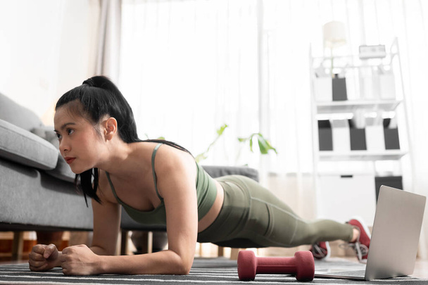 Genç kadın evde dizüstü bilgisayarla planking egzersizi yapıyor. - Fotoğraf, Görsel