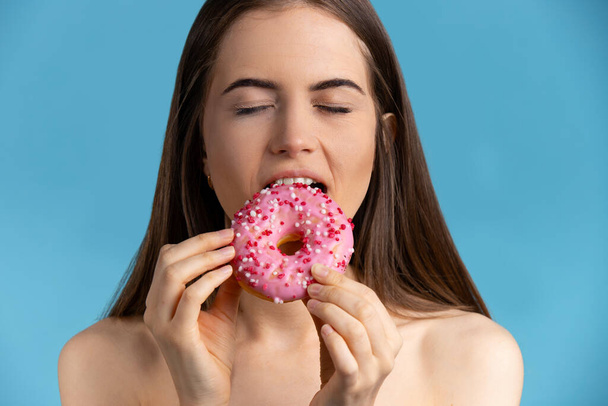 Girl with closed eyes eating pink donuts. Delicious doughnut on isolated blue background - Foto, Bild