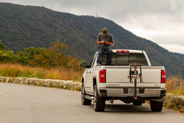 Shenandoah Valley, VA, USA, 09 / 27 / 2020: Egy férfi van a csomagtartóban egy fehér GMC Sierra pickup teherautó ül a vezetőfülkében játszik a telefonjával. A jármű egy festői kilátónál parkol.. - Fotó, kép