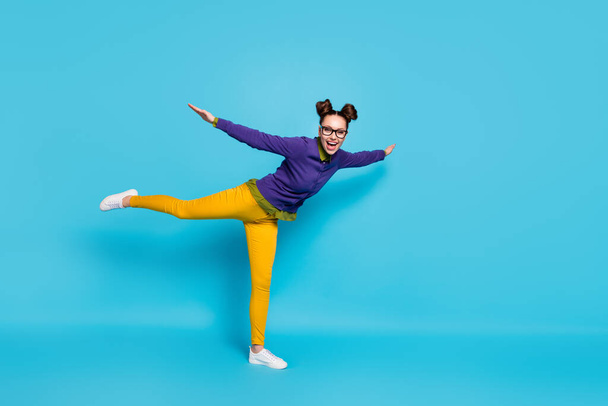 Full length profile photo of pretty crazy lady two buns weekend rejoicing spread arms like wings raise leg bird like wear specs shirt pullover pants isolated blue color background - Foto, imagen