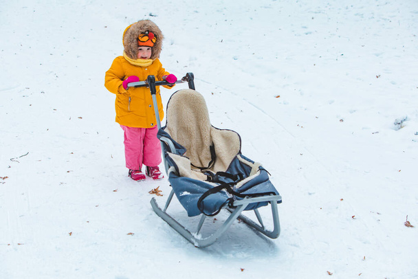 mała uśmiechnięta dziewczyna z saniami w śnieżny zimowy dzień - Zdjęcie, obraz
