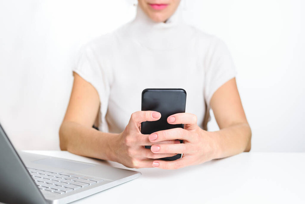 Kaukasische vrouw in witte kleren met een smartphone op kantoor. concept van nieuwe technologieën en afleiding - Foto, afbeelding