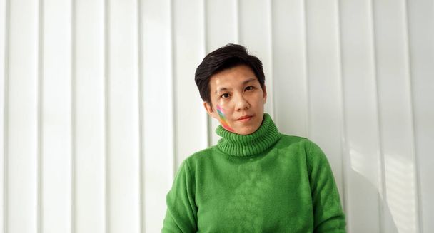Asian ethnic handsome tomboy green sweater with pride flag paint on face support LGBT and transgender - 写真・画像