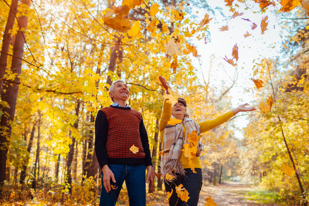 Fall season. Family couple throwing leaves in autumn forest. Senior people having fun outdoors enjoying nature playing games - Photo, Image
