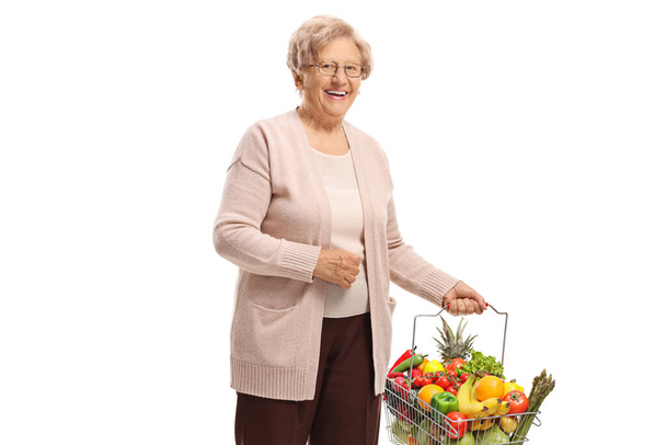 Elderly lady with a shopping basket full of groceries isolated on white background - Fotoğraf, Görsel