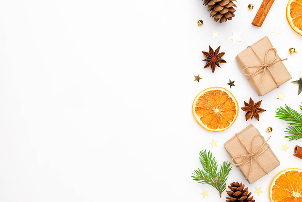 Christmas frame. Gift with fir tree, dry orange, cinnamon sticks, pine cones, star anise, baubles, confetti on white background. - Фото, зображення