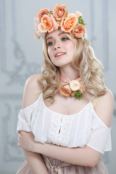 Portrait of a cute happily smiling blonde girl wearing a wreath of tea roses. - Foto, immagini