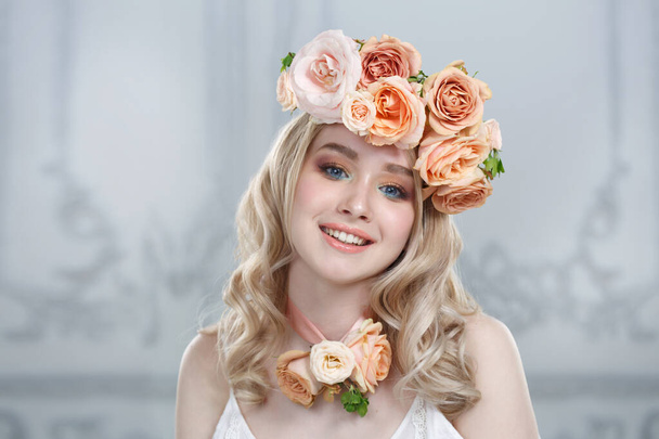 Portrait of a cute happily smiling blonde girl wearing a wreath of tea roses. - Zdjęcie, obraz