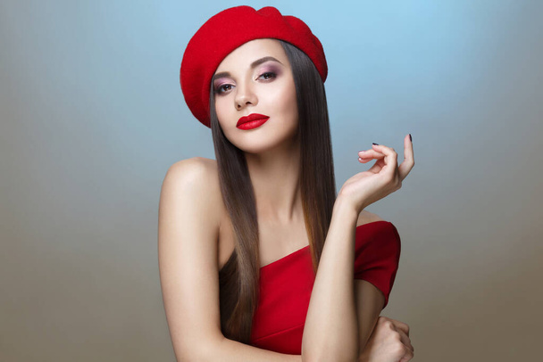 Beautiful brunette in a red beret in an elegant pose on a blue background. - Фото, изображение