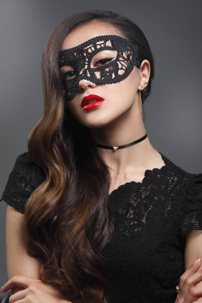 Beauty portrait of a gorgeous girl in a lace mask with red lipstick on lips isolated on a gray background. - Foto, afbeelding
