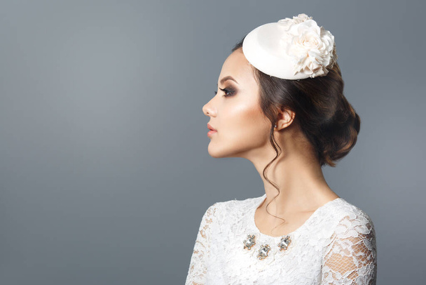 Schönheitsporträt einer niedlichen brünetten Braut mit dekorativem Hut im Profil isoliert auf grauem Hintergrund. - Foto, Bild