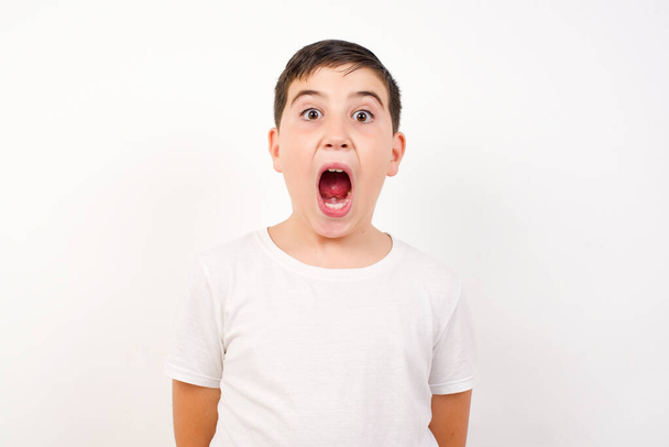 Emotional attraktiver Junge mit geöffnetem Mund äußert große Verwunderung, posiert vor weißem Hintergrund, starrt in die Kamera. Unerwartete schockierende Nachrichten und menschliche Reaktionen. - Foto, Bild