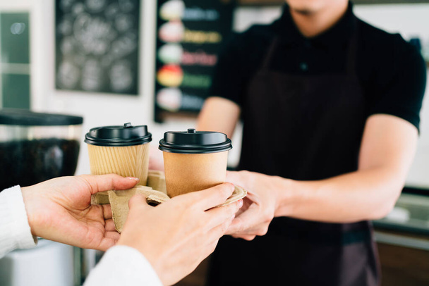 Barista maschile che serve caffè in tazze usa e getta di carta da asporto nella caffetteria. Piccola impresa verde durante la pandemia di coronavirus.  - Foto, immagini