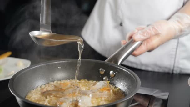 Heerlijke zeevruchten risotto koken in koekenpan. Neergeschoten in slow motion. Visbouillon dat uit de pan wordt gegoten. Traditionele Italiaanse keuken. Vol hd - Video