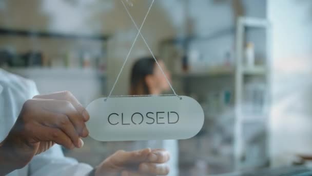 Nierozpoznawalny człowiek obracający tablicę z zamkniętego do otwartego na drzwiach apteki - Materiał filmowy, wideo