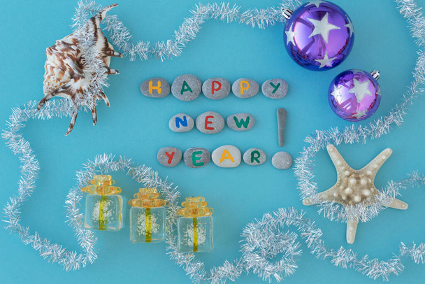 flat lay of inscription new year made with colorful letters on gray sea stones,  sea shells and stars lie arround and long siver tinsel . Greeting travelling concept.  - Φωτογραφία, εικόνα