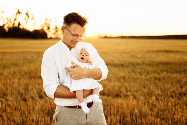Handsome father with adorable little daughter at the field, caring dad hold cute newborn baby girl in arms, tender family moments, parenting and fatherhood concept  - Photo, Image