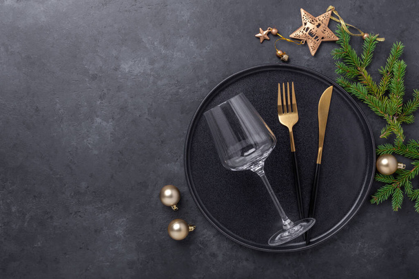 Christmas table setting with black ceramic plate, glass and gold decoration on black stone background. Top view. Copy space - Image - Foto, Imagem