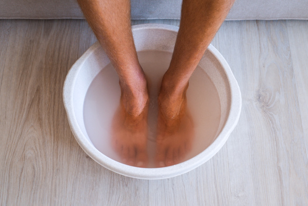 Baño hecho por el hombre con agua caliente y bicarbonato de sodio para sus pies. Remojo casero del baño para la piel seca de los pies - Foto, Imagen