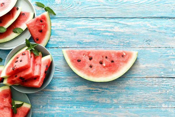 Sliced ripe watermelon witn mint on a colored plates. Big slice of watermelon in center on an blue rustic wood background. top view witn copy space. Summer time concept - Photo, image