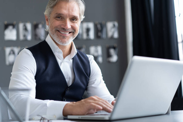 Soustředěný v práci. Šťastný dospělý muž v plném obleku pomocí notebooku při práci v moderní kanceláři. - Fotografie, Obrázek