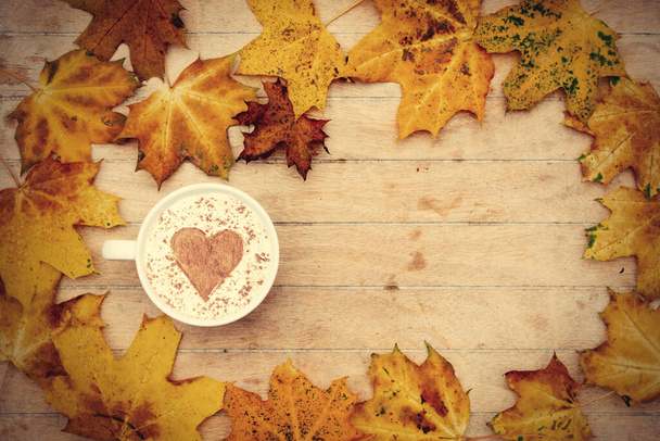 Masanın üzerinde tarçınlı bir kalp ve akçaağaç yapraklı bir fincan kahve. - Fotoğraf, Görsel
