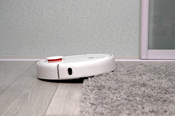 white Robot vacuum cleaner drives on carpet. Overcoming obstacles with robot vacuum cleaner. ideal cleaning of house with modern wireless appliances. concept of smart home. - Foto, Imagen