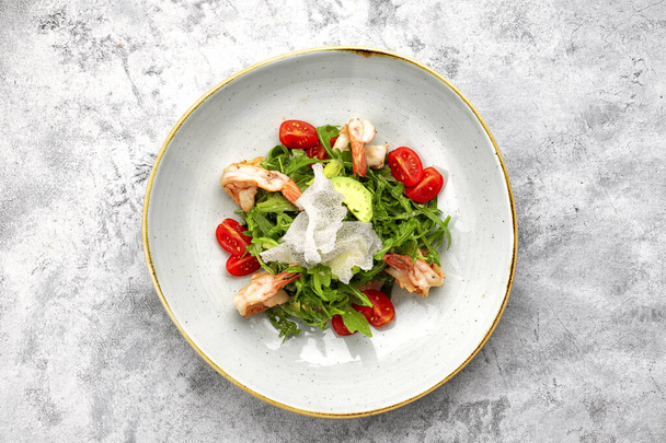 Салат с креветками, помидорами и рукколой, на белой тарелке, на светлом фоне - Фото, изображение
