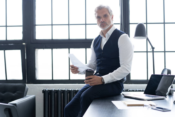 Pensive handsome matured confident businessman in trendy formal wear checking accounting report - 写真・画像
