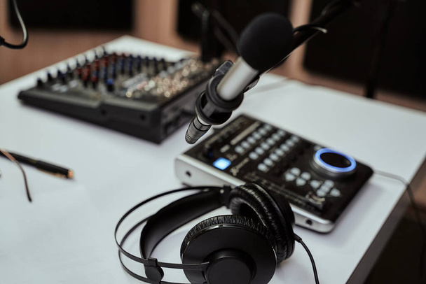 Pracoviště moderátora rádia. Zblízka sluchátka, mikrofon a mixážní pult na stole v nahrávacím studiu nebo vysílací místnosti - Fotografie, Obrázek