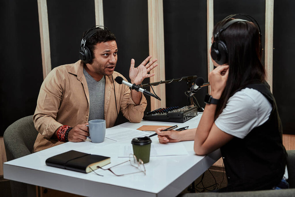 Portait δύο ραδιοφωνικών παρουσιαστών, άνδρας και γυναίκα που συνομιλούν μεταξύ τους ενώ συντονίζουν ένα live show στο studio - Φωτογραφία, εικόνα