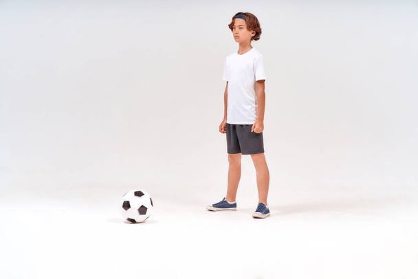 Nuori jalkapalloilija. Täyspitkä laukaus teini poika pelaa pois pelatessaan jalkapalloa eristetty yli harmaa tausta - Valokuva, kuva