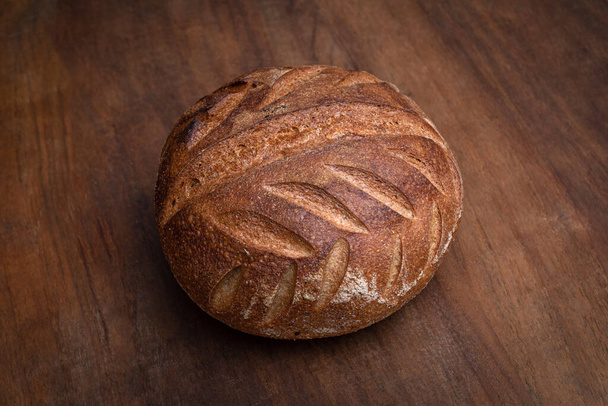 Hustá krusta organický kulatý vesnický chléb na hnědé dřevěné plošině, zblízka. - Fotografie, Obrázek