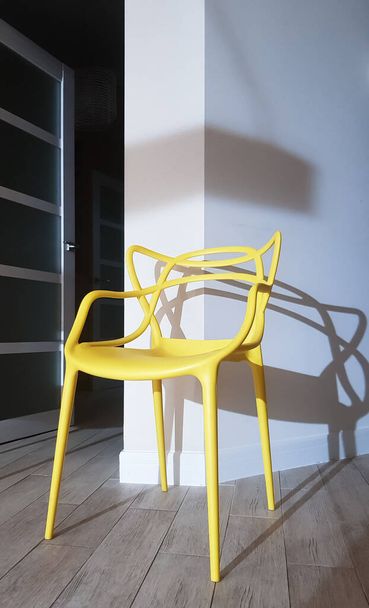 Желтый пластиковый стул возле стены с тенью в интерьере дома - Фото, изображение